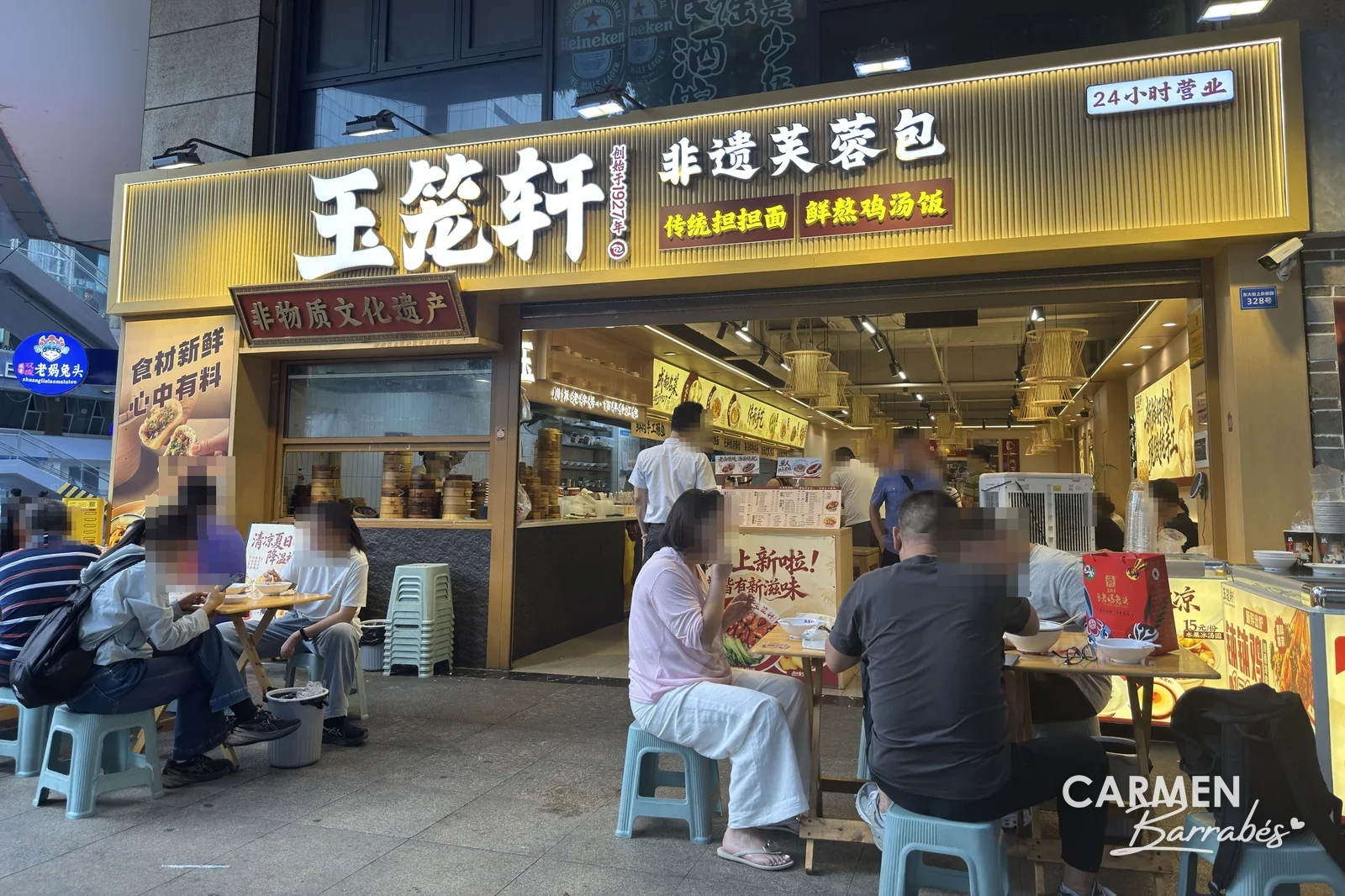 Gente desayunando en taburetes a la puerta de Yulongxuan, en Chengdú, un local de bollos al vapor y dandan mian abierto las 24 horas