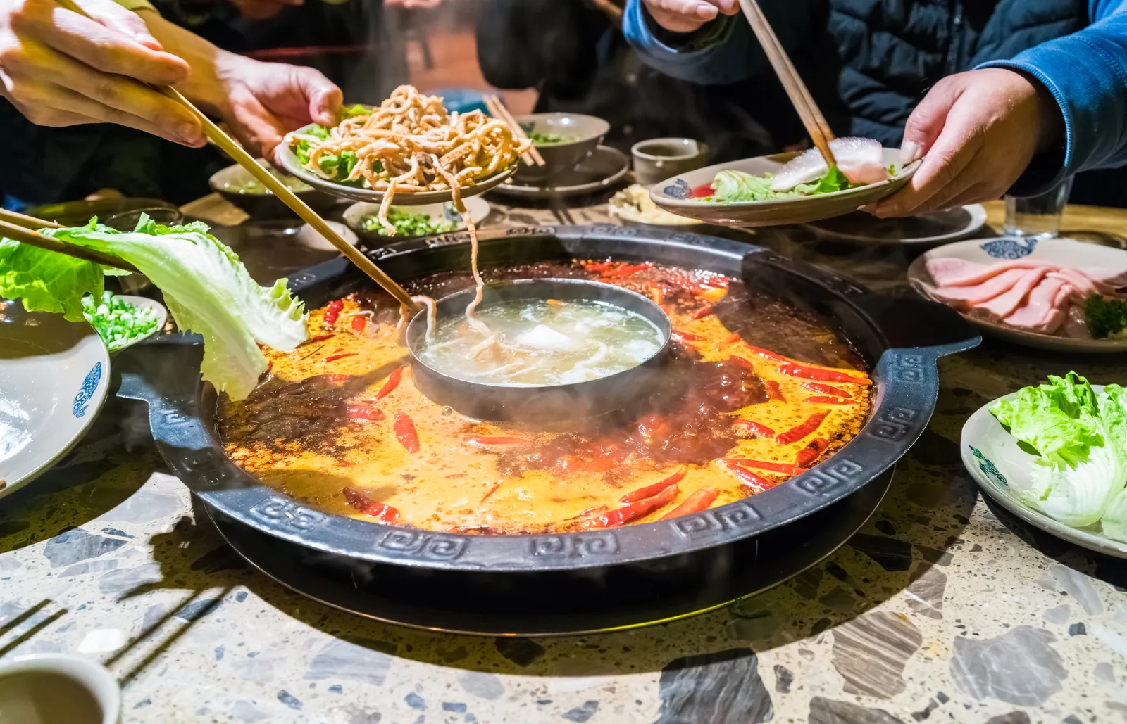 Comensales cocinando en la olla roja de un restaurante de hotpot de Chongqing