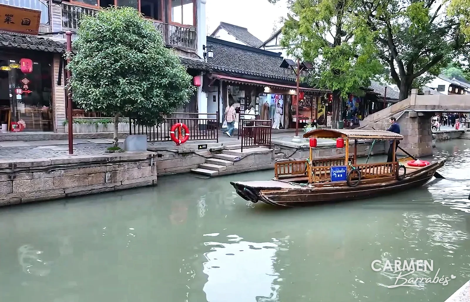 Barca tradicional de madera en un canal estrecho de Zhujiajiao con un puente de piedra al fondo