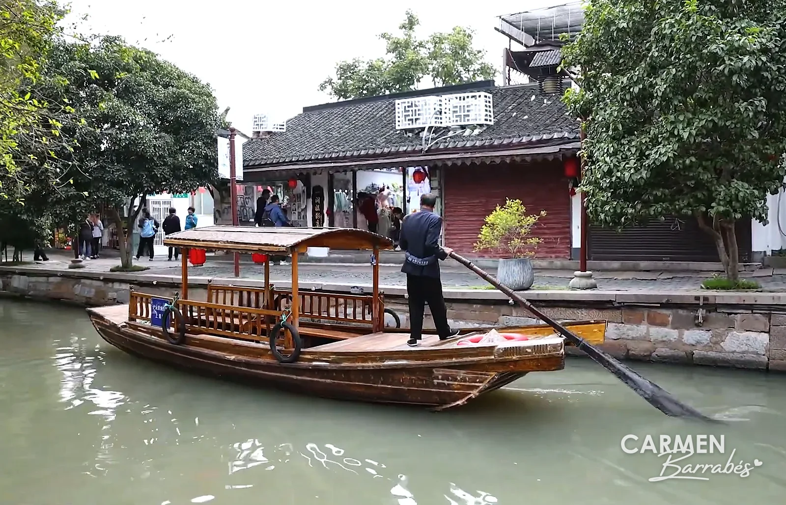 Barquero remando de pie en una barca de madera por un canal de Zhujiajiao