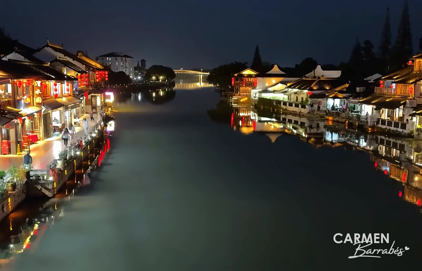 El canal de Zhujiajiao al anochecer, con las casas iluminadas reflejadas en el agua y un puente al fondo