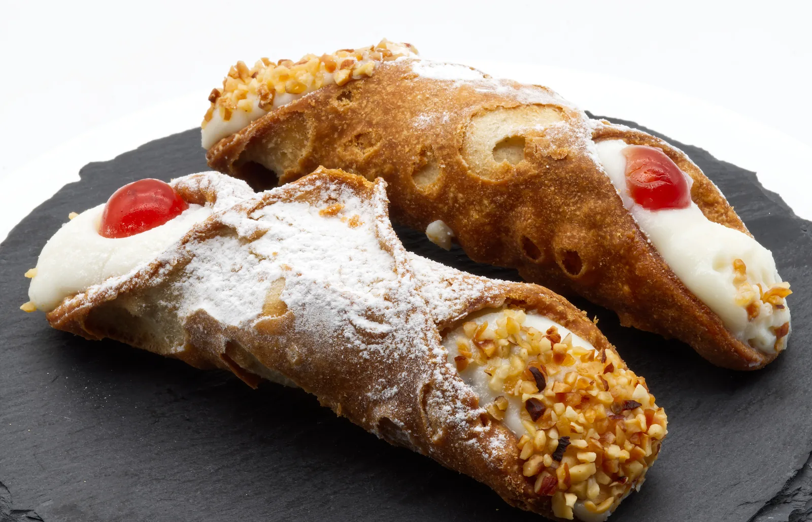 Dos cannoli sicilianos rellenos de requesón, con pistacho y una guinda confitada