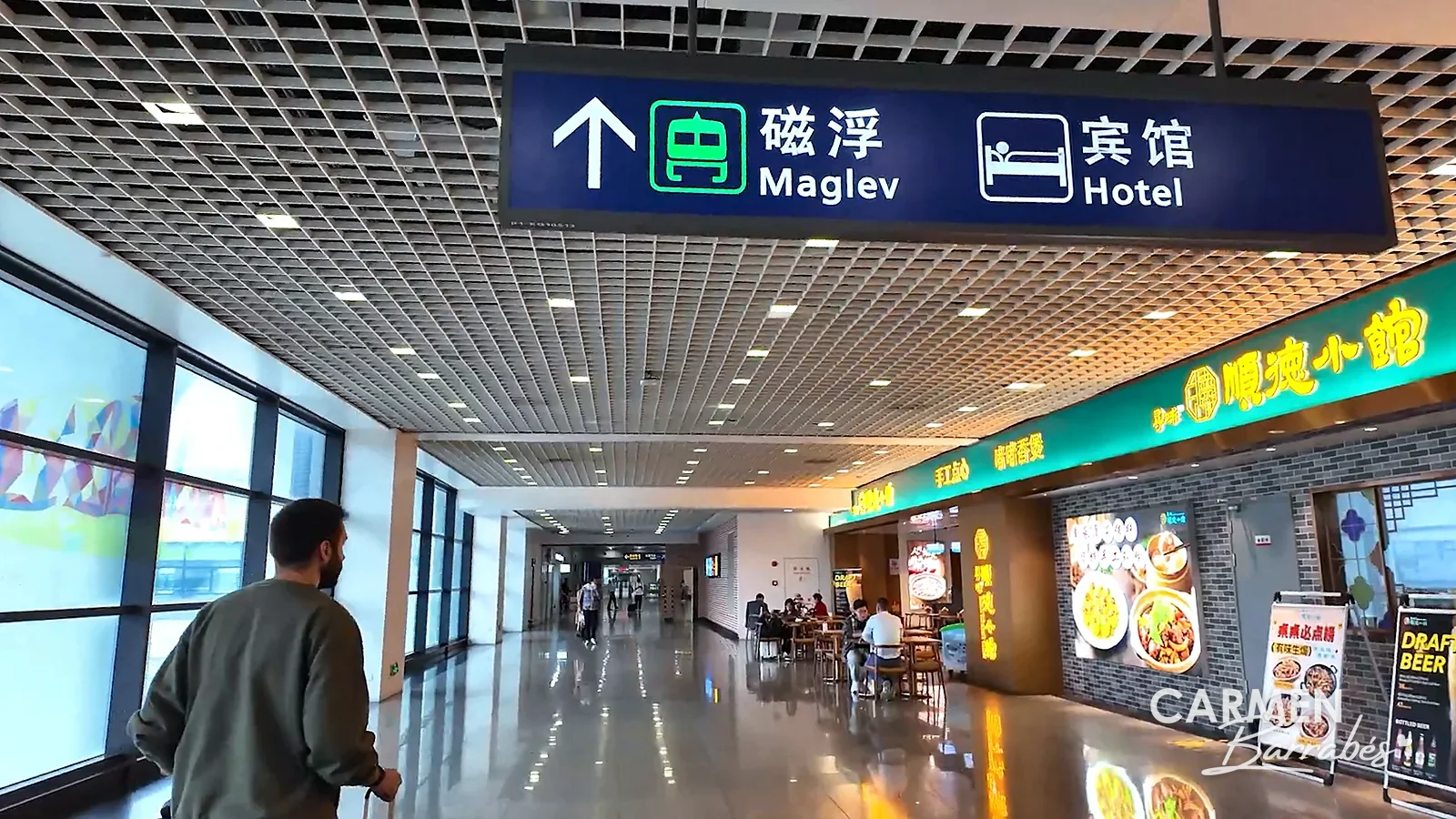 Cartel con flecha hacia el Maglev (磁浮) y los hoteles en un pasillo de la terminal del aeropuerto de Pudong