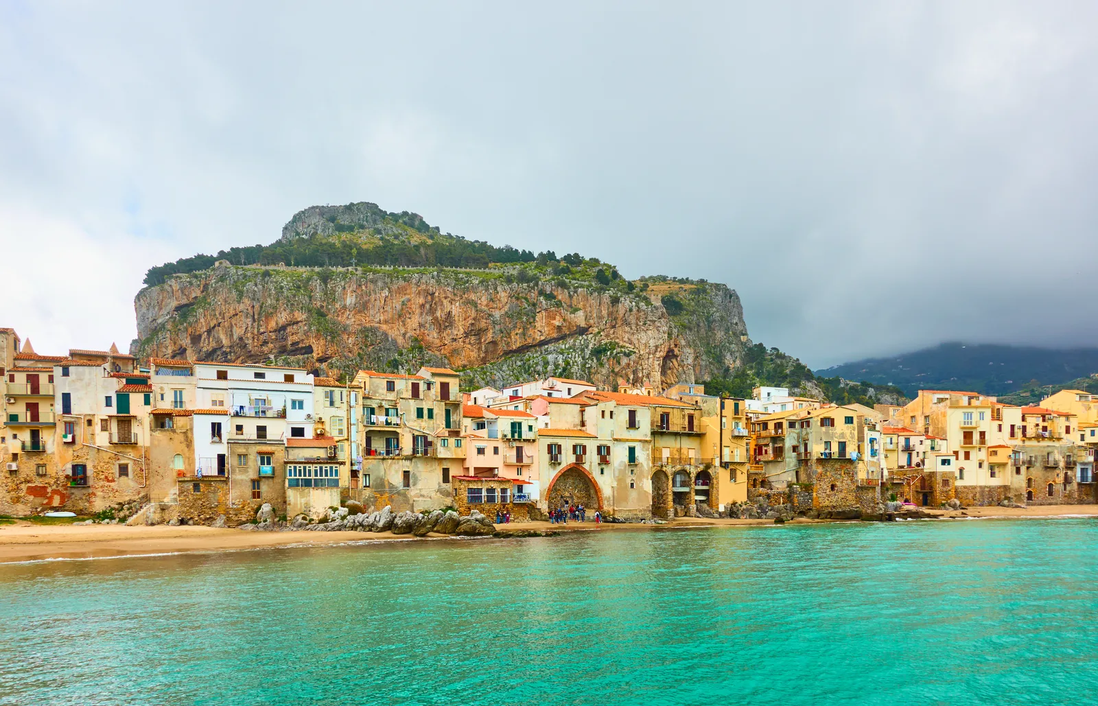 Cefalú con el agua turquesa delante, las casas del casco antiguo y La Rocca detrás