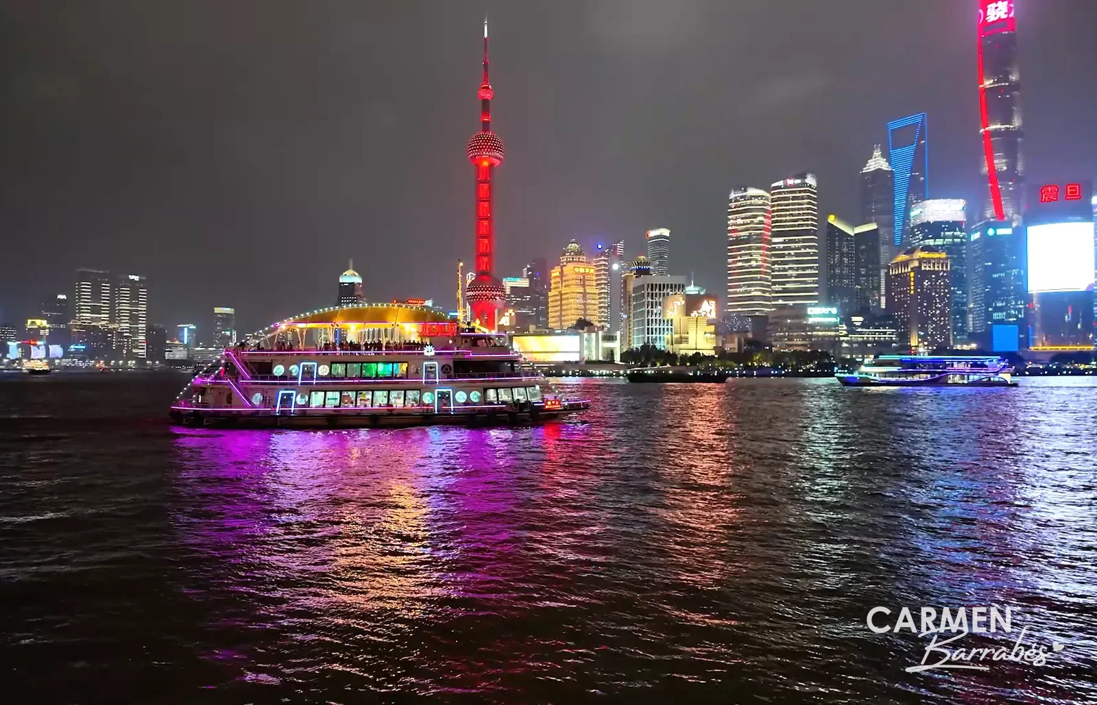Barco de crucero iluminado en el río Huangpu frente a los rascacielos de Lujiazui