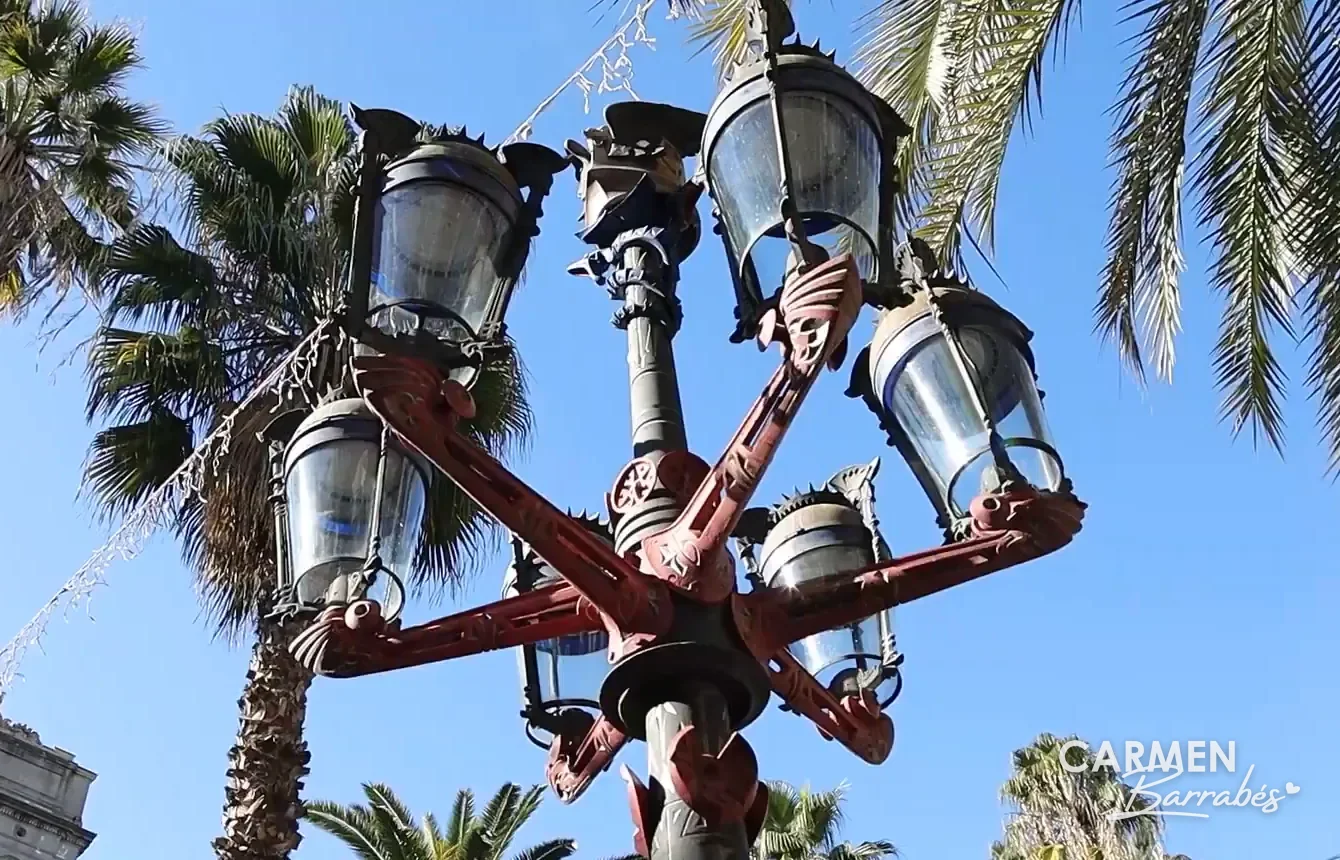Una de las farolas de Gaudí entre las palmeras de la plaza Real de Barcelona
