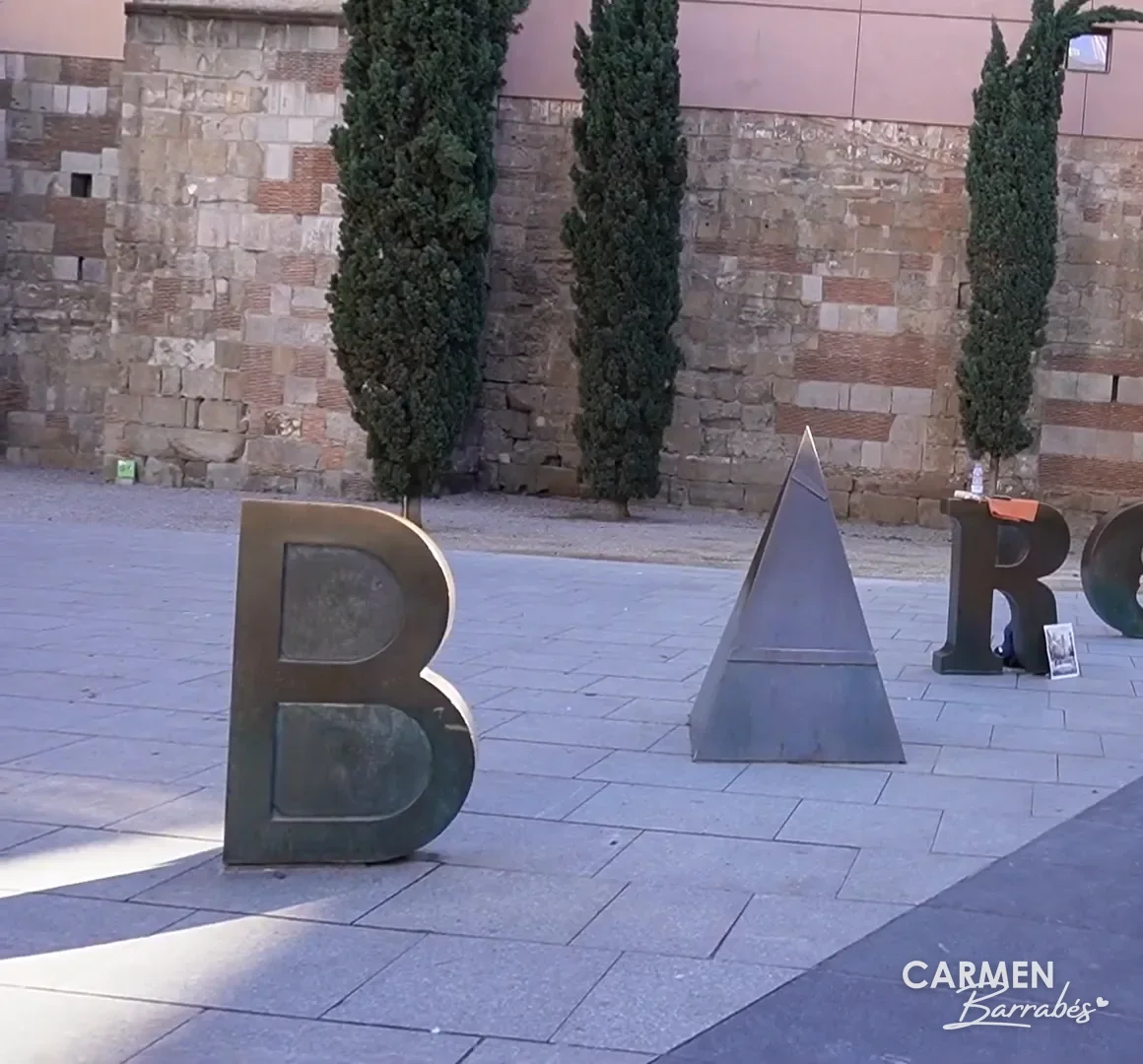 Las letras Barcino de Joan Brossa delante de la muralla romana en la plaza Nova de Barcelona