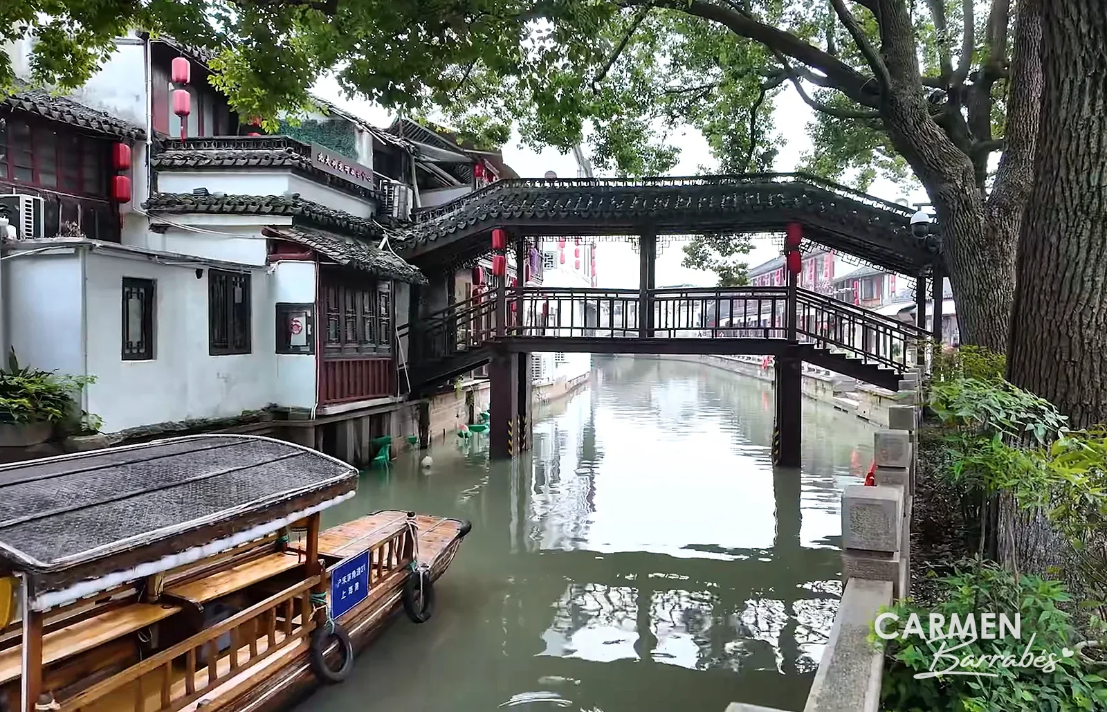 Puente cubierto de madera sobre un canal de Zhujiajiao, junto a un árbol grande y barcas amarradas