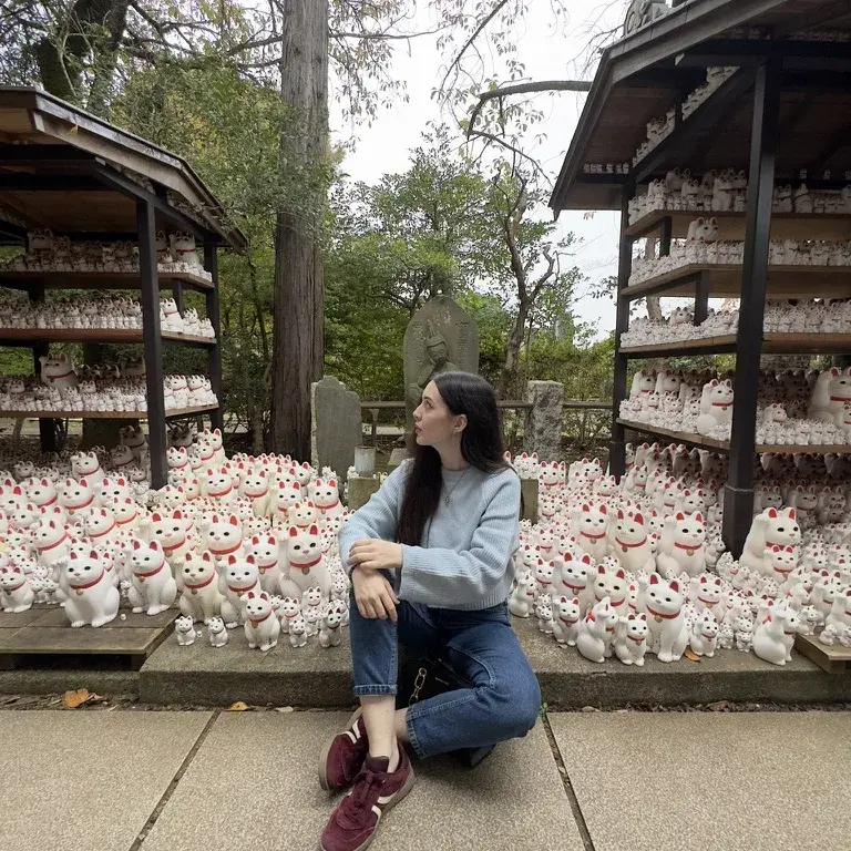 Carmen sentada entre gatos de la suerte en un santuario de Japón