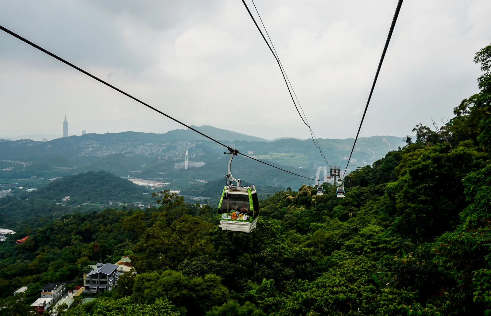 Cabina del teleférico de Maokong sobre colinas verdes, con la Taipei 101 al fondo