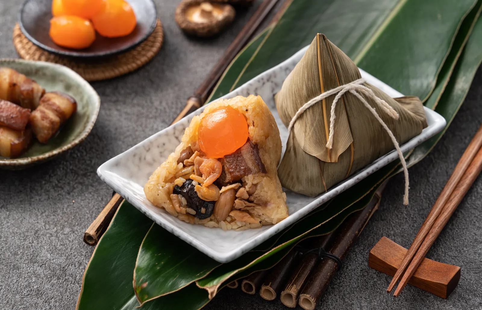 Zongzi de arroz glutinoso envueltos en hoja de bambú, uno abierto con panceta y yema de huevo salada